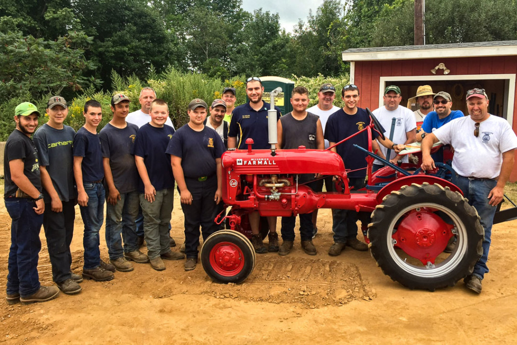 The whole tractor team standing a Farmall they restored.